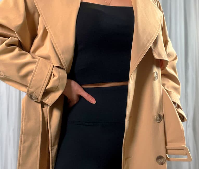 Cropped woman wearing black leggings and a black top layered with a trench coat