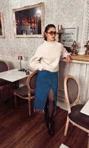 A woman wearing a denim midi skirt with a white sweater