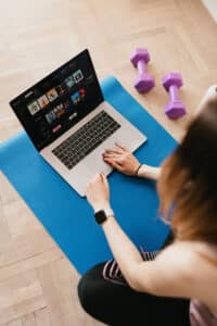 A woman sitting on a yoga mat watching Netflix.