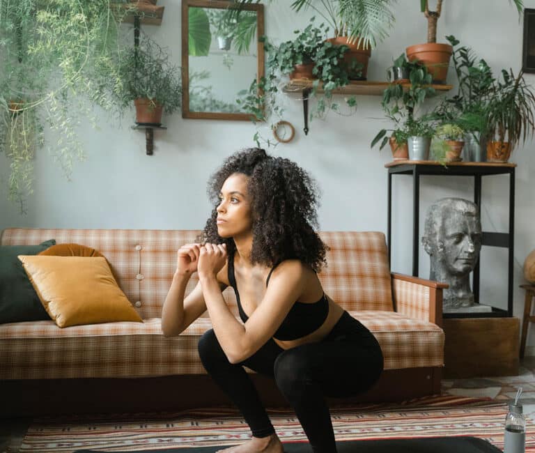 A woman in a black workout set doing squats in her living room.