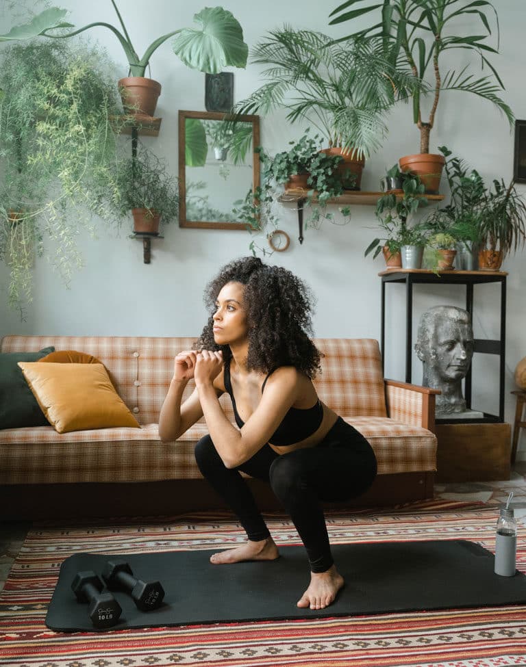 A woman in a black workout set doing squats in her living room.