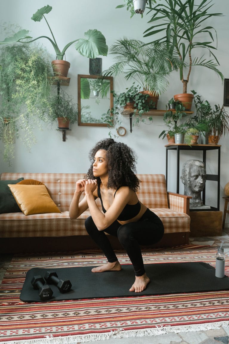 A woman in a black workout set doing squats in her living room.