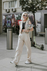 A woman wearing beige straight-leg pants with a matching waistcoat holding some magazines in her arms