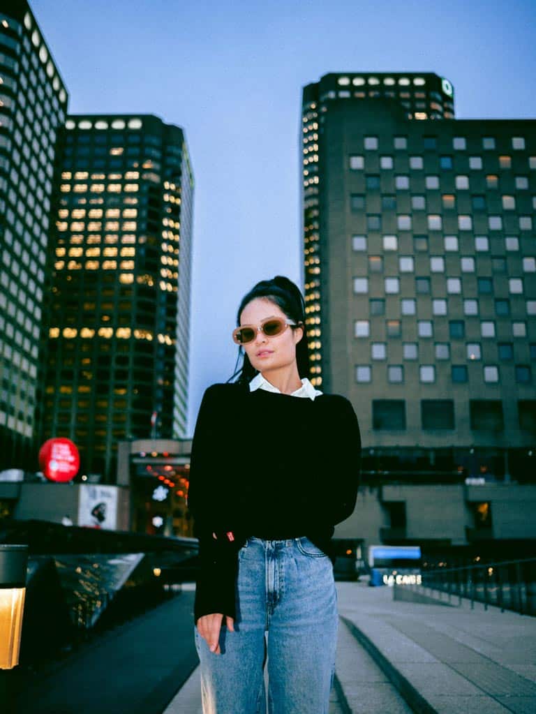 Cropped woman wearing a black crew-neck jumper with jeans and beige sunglasses