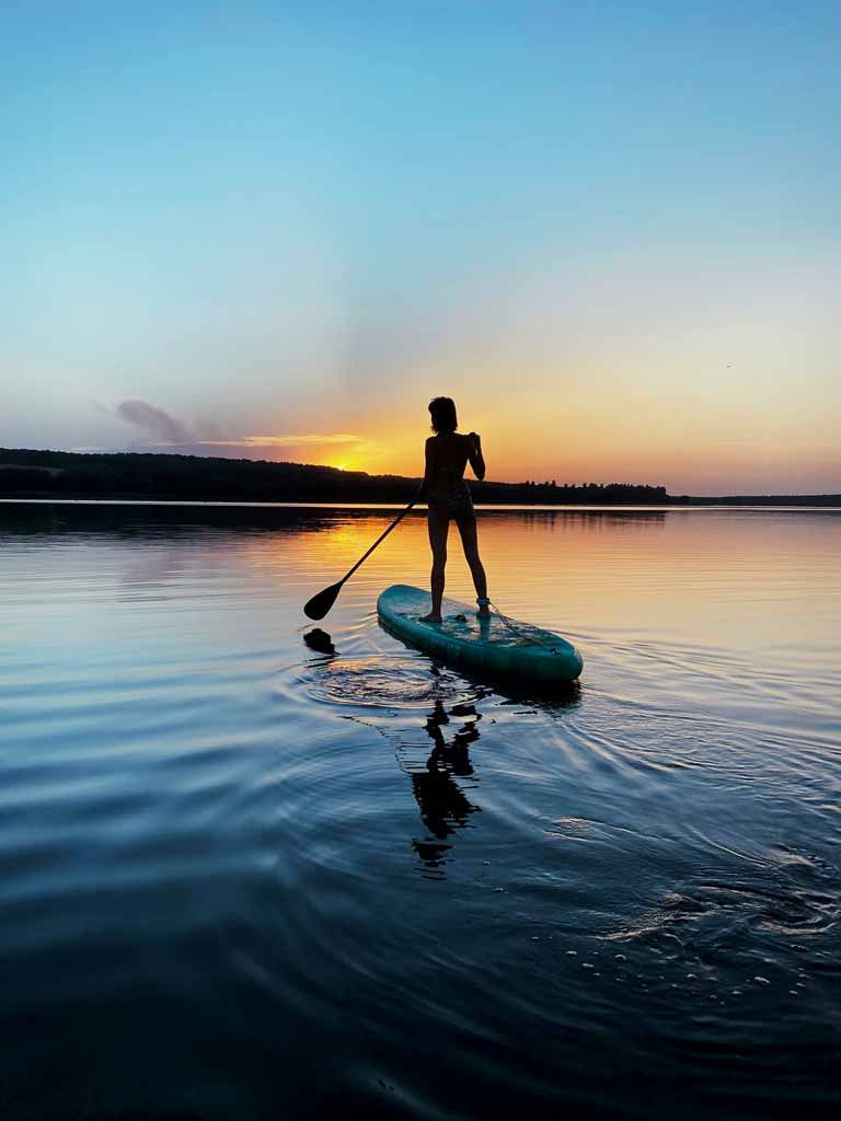 A woman doing standing-up paddle boarding during a sunset