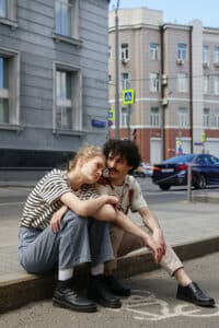 A couple sitting on the edge of the sidewalk.