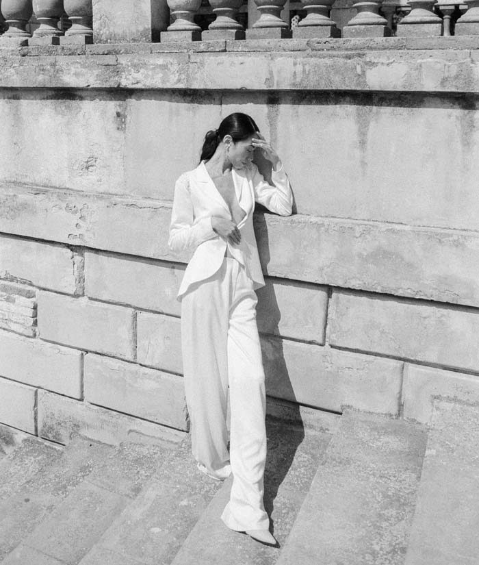woman wearing a white suit posing in front of stone balustrades